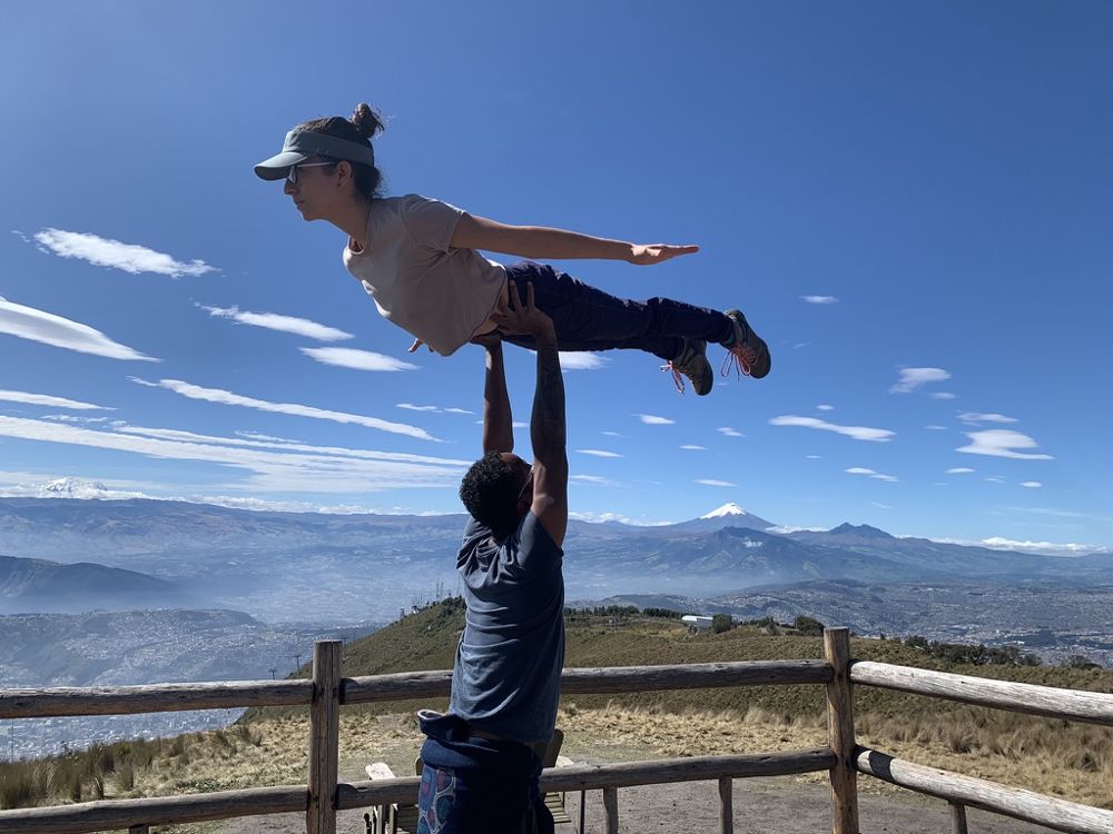 Josue basing an AcroYoga flyer on a lookout above Quito, with the Andes and a snow-capped volcano behind